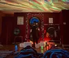 The image shows a dimly-lit room with a cosmic star projector effect on the ceiling while several people lay on mats under blankets and a person at the front appears to be performing a sound healing or meditation session with large gongs