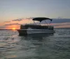 A pontoon boat floats on calm waters against the backdrop of a beautiful sunset