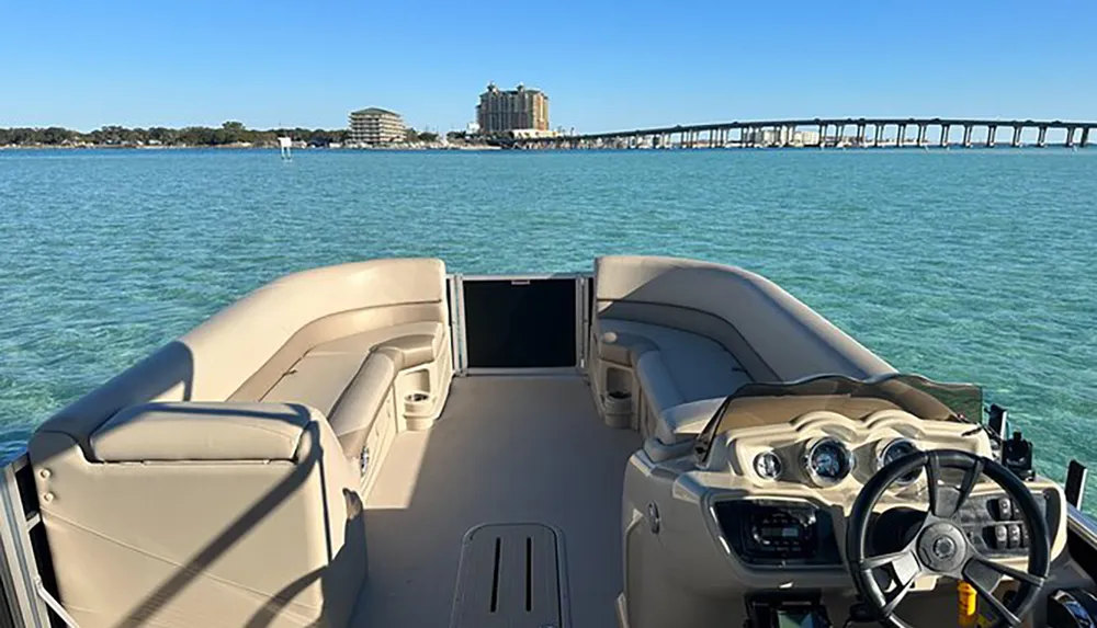 The image shows the interior of a pontoon boat overlooking a turquoise waterway with a bridge and buildings in the distance suggesting a leisurely day on the water