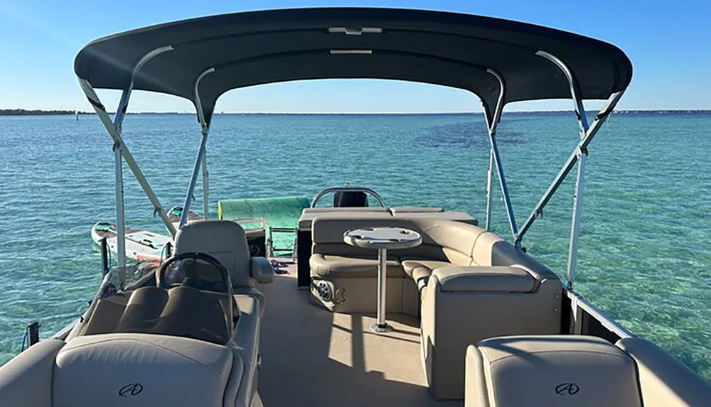 The image shows an empty pontoon boat floating on clear turquoise water under a bright blue sky