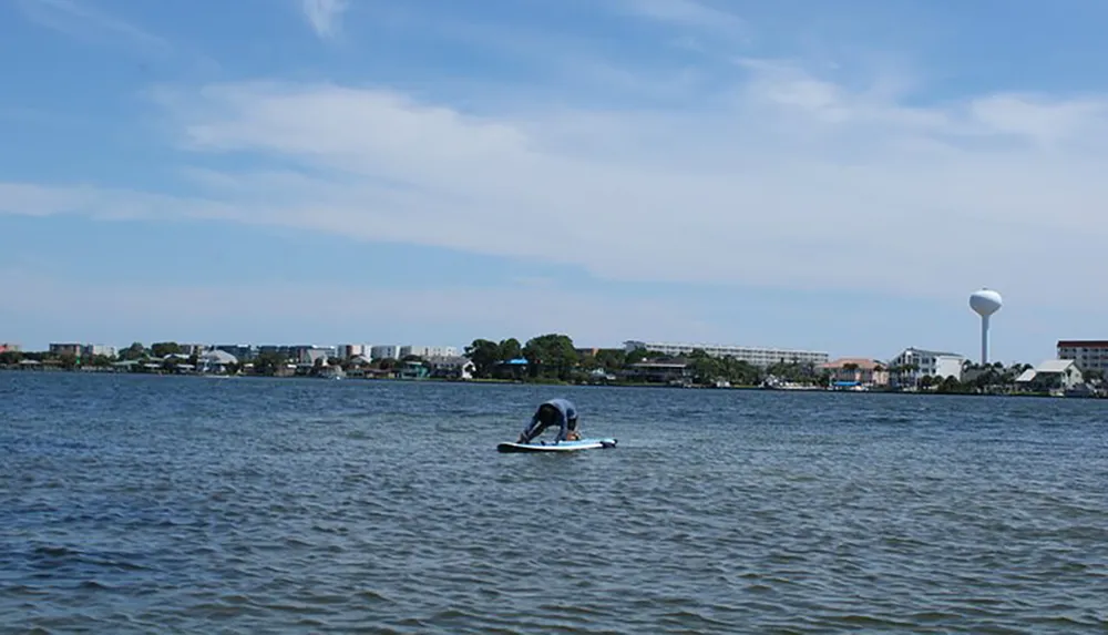 A person is paddleboarding on a calm body of water with a coastal cityscape in the background