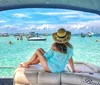 A person sits on the stern of a boat gazing at a vibrant beach scene with clear turquoise water and numerous boats and people enjoying water activities