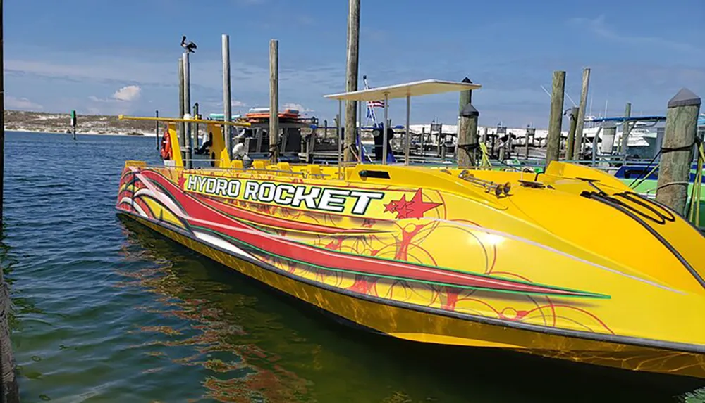 A bright yellow speedboat named HYDRO ROCKET adorned with red and green graphics is docked in a marina on a sunny day