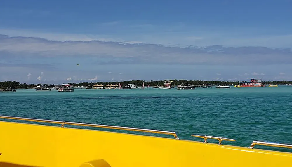 A view from a boat showing a vibrant turquoise sea scattered boats and coastal buildings under a partly cloudy sky