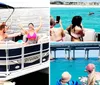 Two people are photographing a dolphin leaping out of the turquoise waters near a beach from a boat