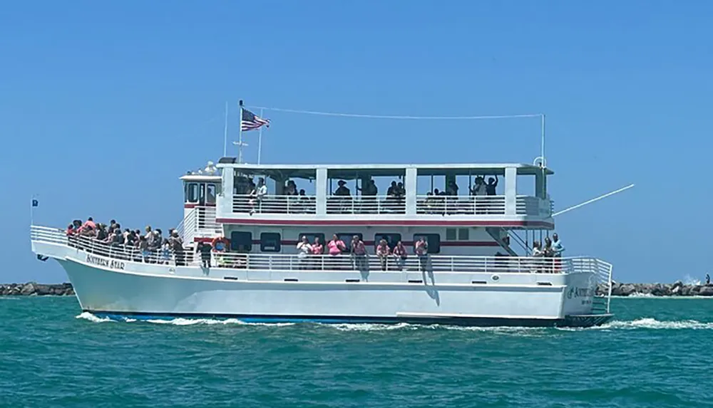 A group of passengers enjoys a sunny day out on the deck of a sightseeing boat cruising through blue waters