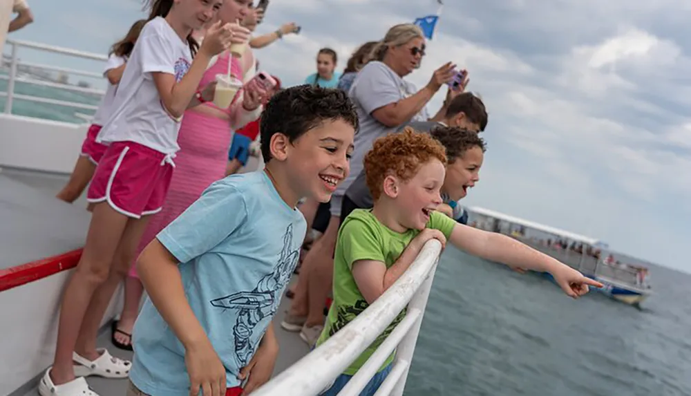 A group of excited children leans against the railing of a boat pointing and looking at a view or object of interest at sea