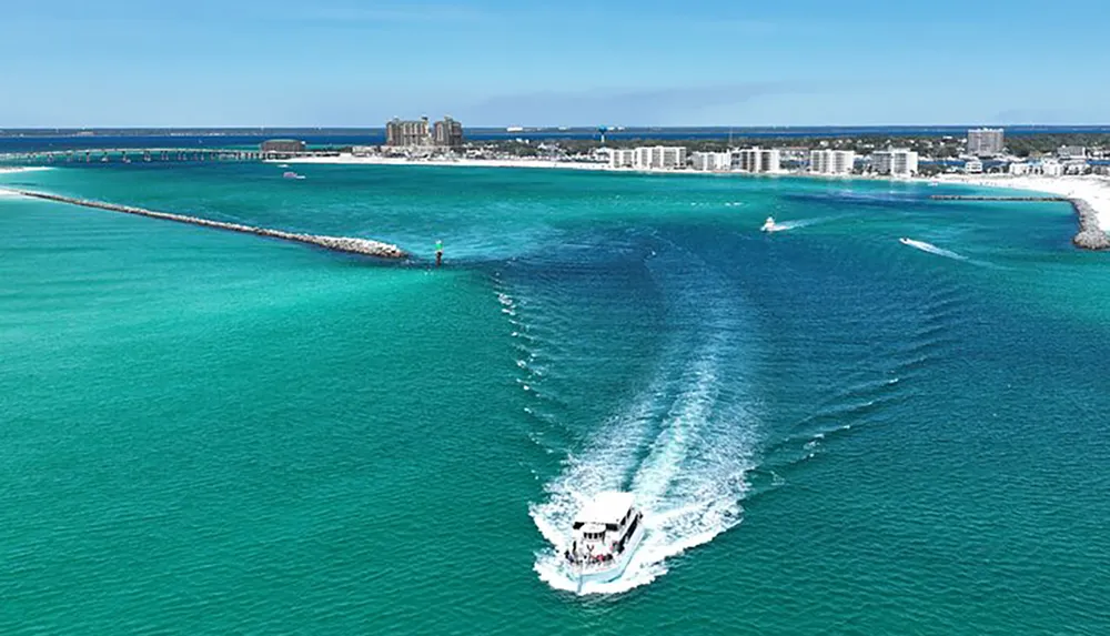 A boat is creating a wake as it moves through turquoise waters near a breakwater with a coastal city skyline in the background