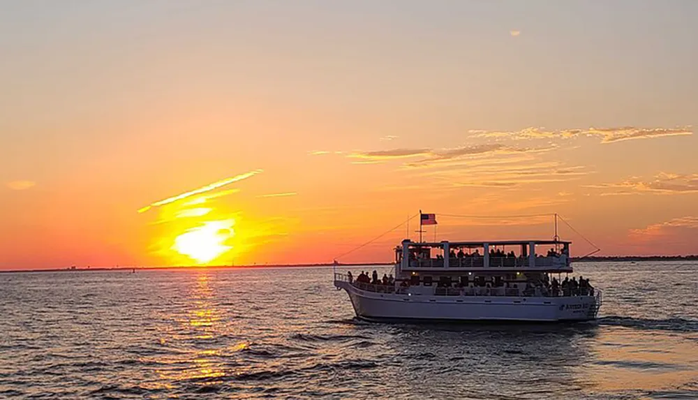 A tour boat is filled with passengers as they enjoy a vivid sunset over the water