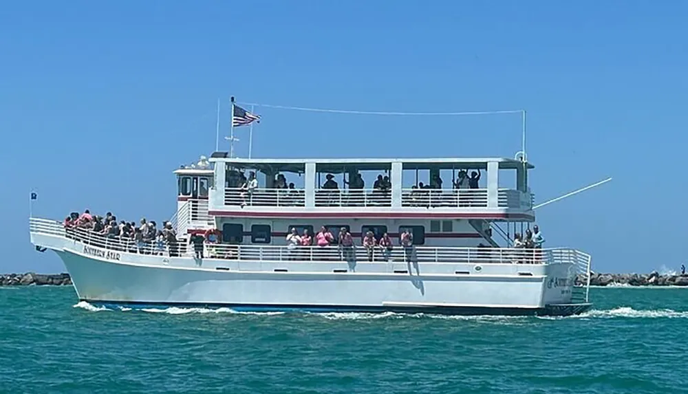 A tour boat full of passengers is sailing near the coast under a clear blue sky