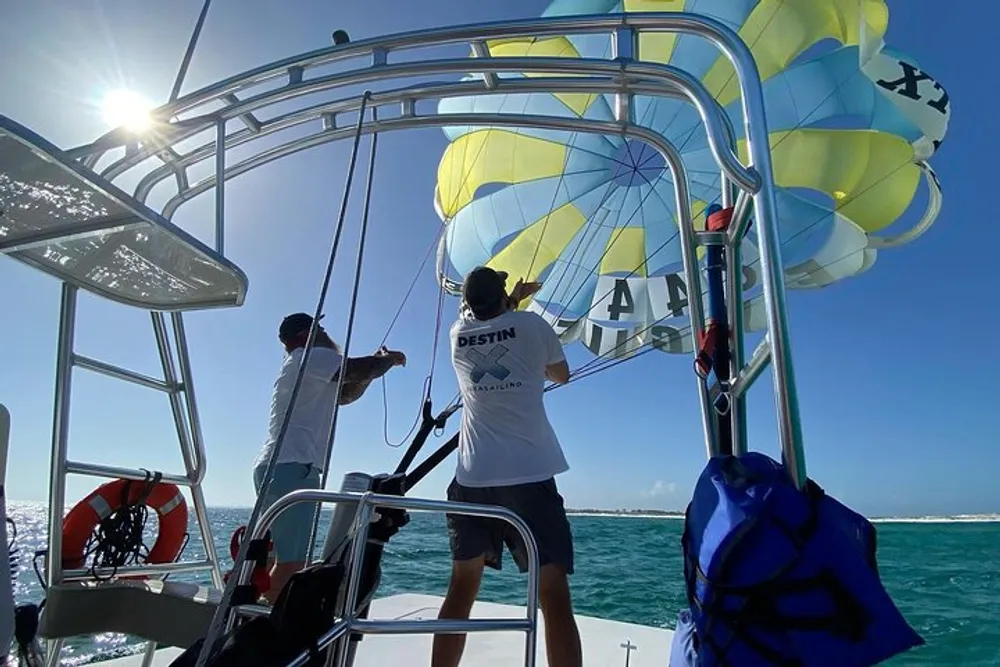 Two people on a boat are managing a parasail against a backdrop of blue sky and sea