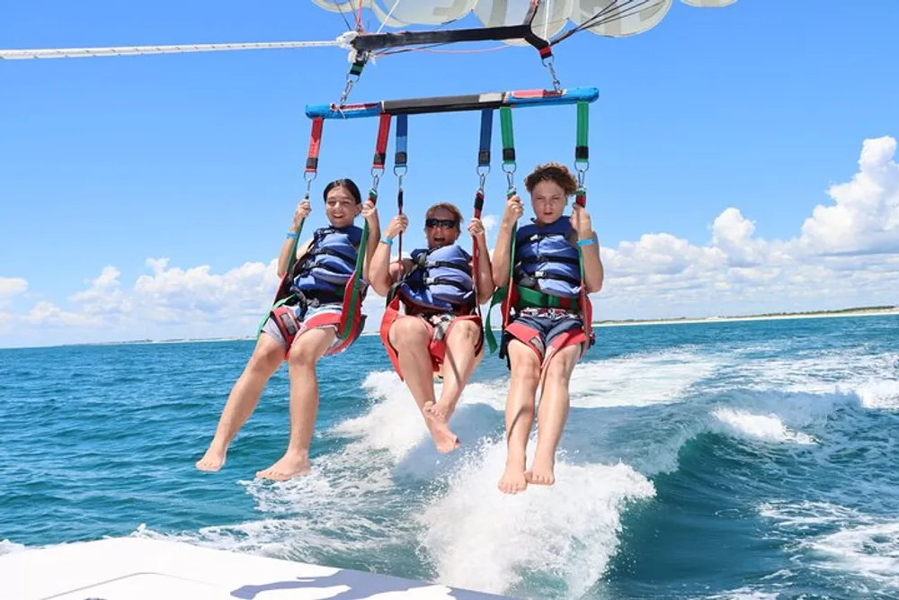 Three individuals are enjoying a parasailing adventure over the ocean on a sunny day