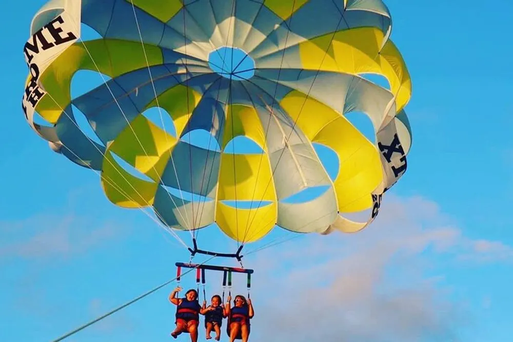 Three individuals are enjoying a parachute ride against a clear blue sky