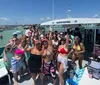 A group of people is enjoying the clear shallow waters next to a boat named BIKKINI BOTTOM with some sitting on a paddleboard and others standing or preparing to swim