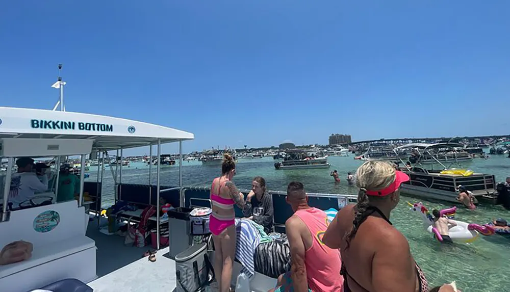 A group of people enjoy a sunny day on a boat named BIKKINI BOTTOM surrounded by many other boats on a busy waterway