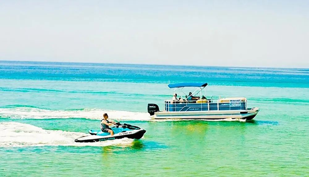 A person is riding a personal watercraft in clear blue waters near a pontoon boat with people on board