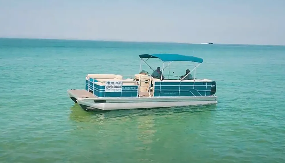 A pontoon boat with a few passengers is floating on calm turquoise waters