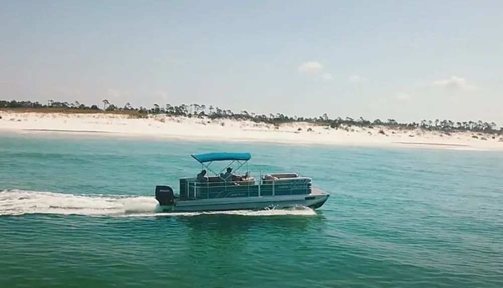 A pontoon boat with a blue canopy is cruising near a beach with white sand and sparse vegetation