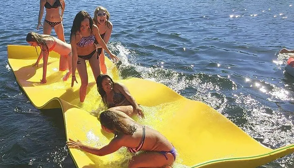 A group of people is enjoying playtime on a large yellow floating mat in the water on a sunny day