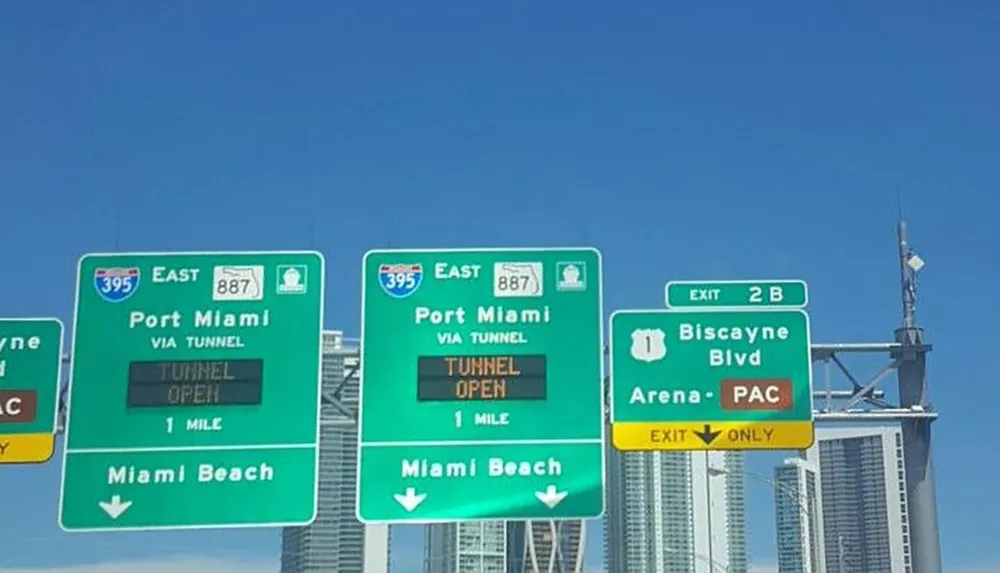 The image shows several road signs indicating directions for East 395 to Port Miami and Miami Beach as well as an exit sign for Biscayne Boulevard near some tall buildings under a clear blue sky