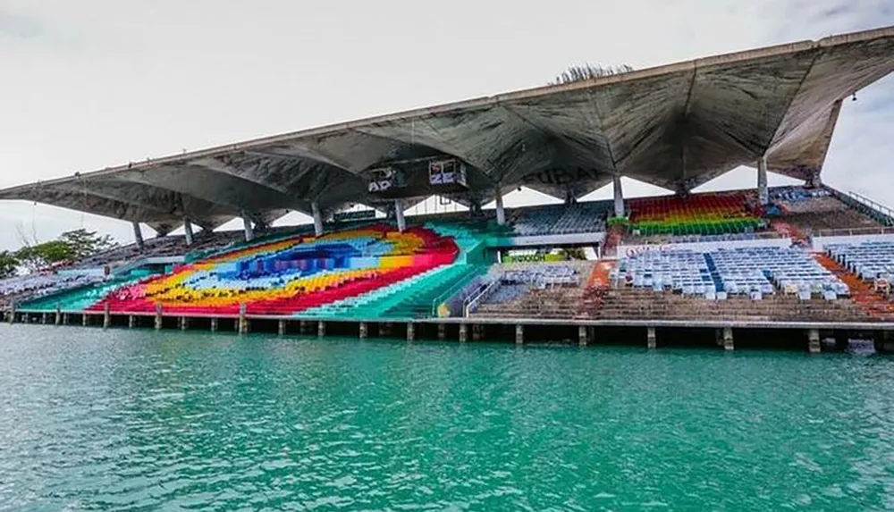 This image shows a colorful stadium with a roof built on a pier over turquoise waters