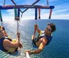 Two people are enjoying themselves while parasailing above a clear blue ocean