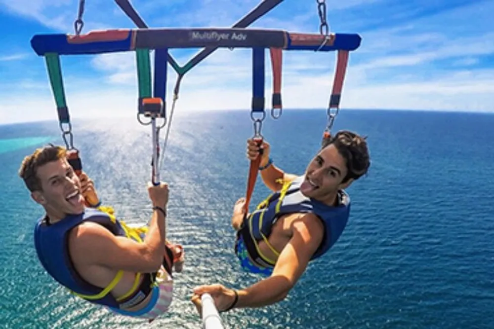 Two people are enjoying themselves while parasailing above a clear blue ocean