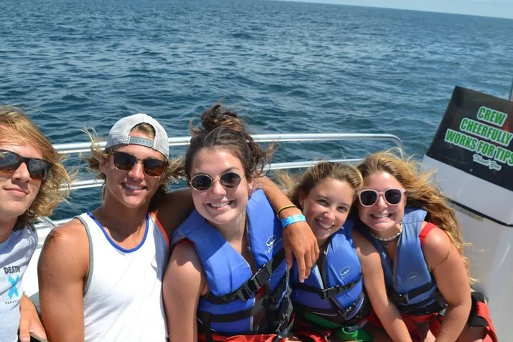 A group of young people wearing life jackets are smiling for the camera on a boat with the ocean in the background