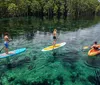 A smiling woman and a young boy are sharing a clear kayak both holding paddles on a calm water body