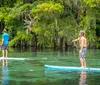 A smiling woman and a young boy are sharing a clear kayak both holding paddles on a calm water body