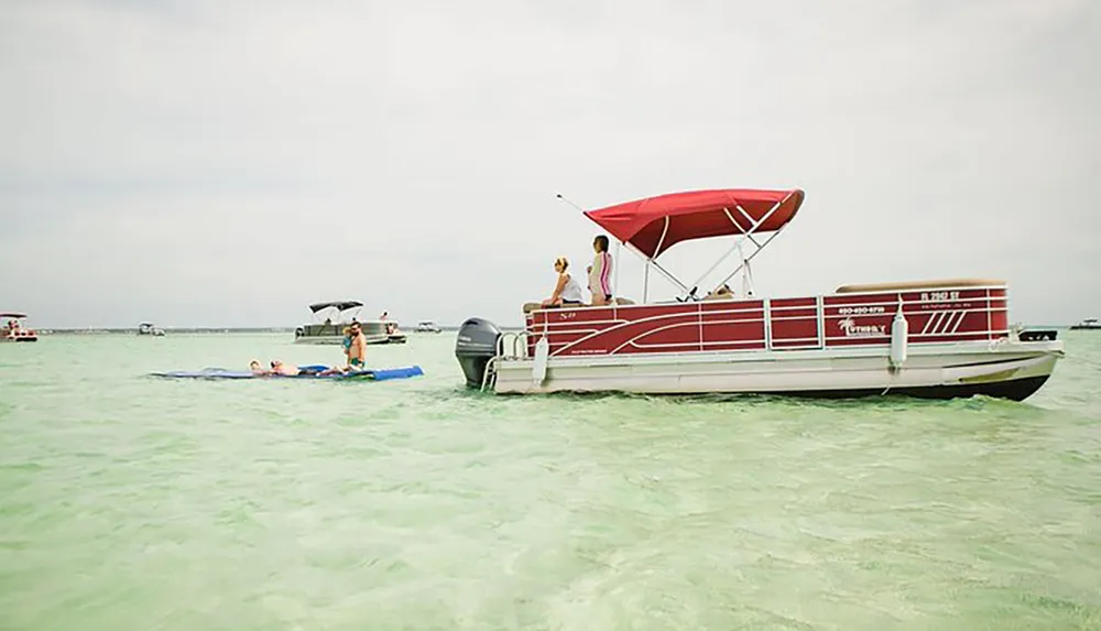 People enjoy leisure activities in and around a pontoon boat on a shallow clear water body