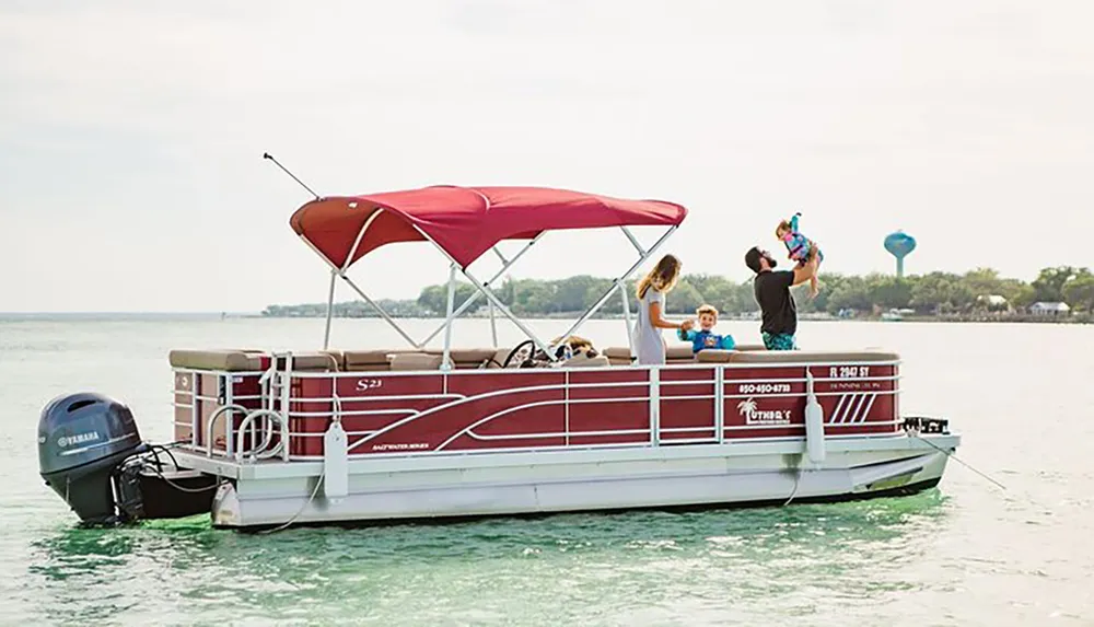 A family enjoys time together on a red and white pontoon boat on a calm body of water