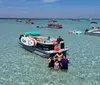 The image shows a lively water scene with people enjoying various activities on boats a floating mat and a paddleboard in clear turquoise waters