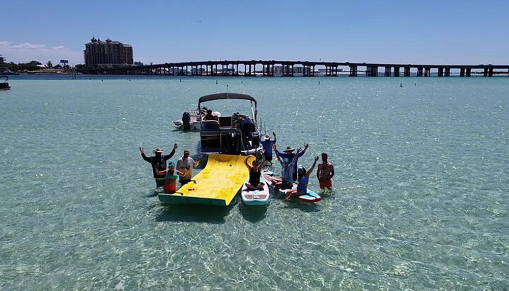 A group of people is enjoying a sunny day on a boat with a yellow slide and in the water near a bridge