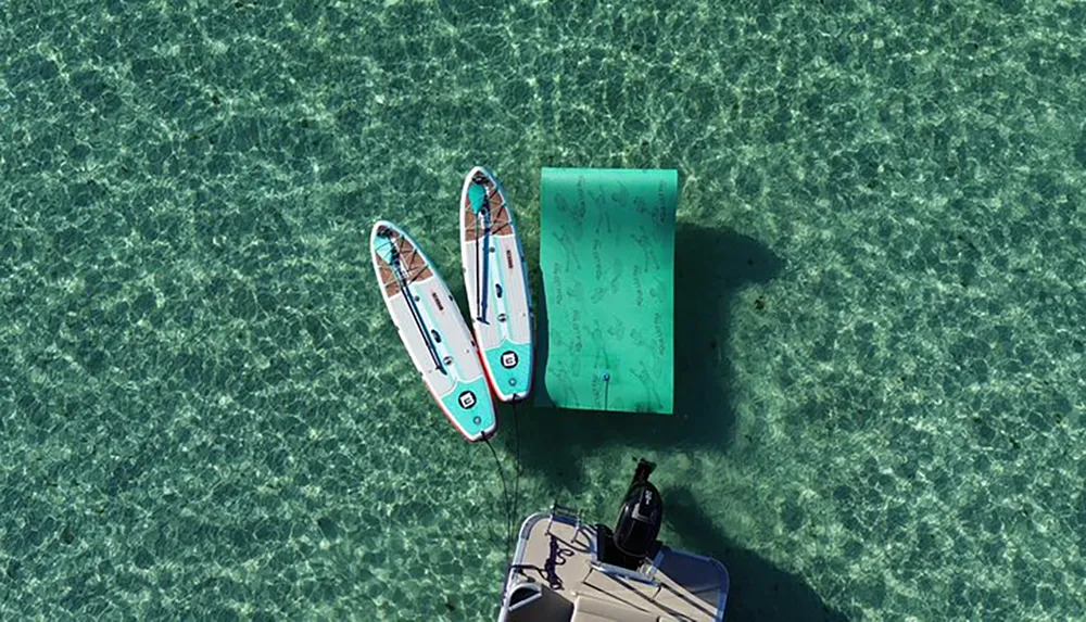 Two paddleboards are moored next to a floating dock above clear turquoise waters with the edge of a boat visible in the foreground