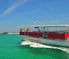 A pontoon boat named SunVenture II is cruising on bright turquoise waters near a sandy coastline with a pier and buildings in the background under a blue sky