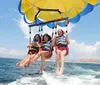 Three individuals are enjoying parasailing above the ocean with smiles on their faces suggesting they are having a great time