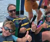 Three individuals are enjoying parasailing above the ocean with smiles on their faces suggesting they are having a great time