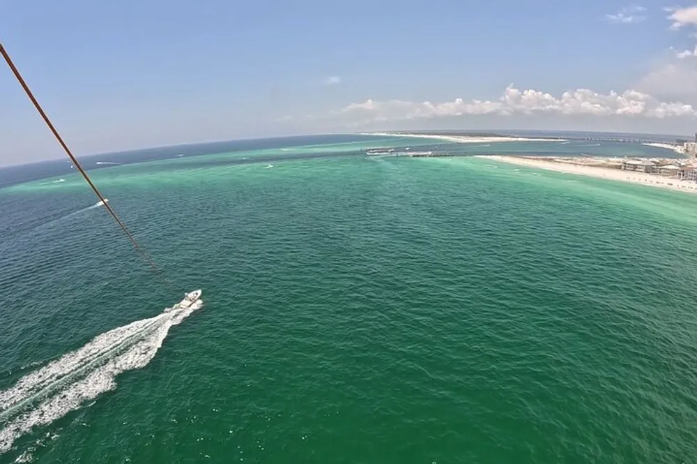 The image shows a view from above of a boat cruising through green waters near a coastline with a parasailing line visible on the left side indicating the photo might have been taken by someone parasailing