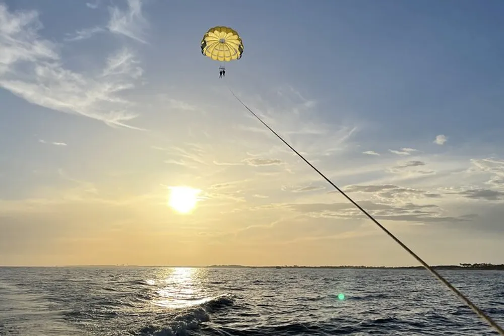 A person is parasailing above the sea against a backdrop of a beautiful sunset