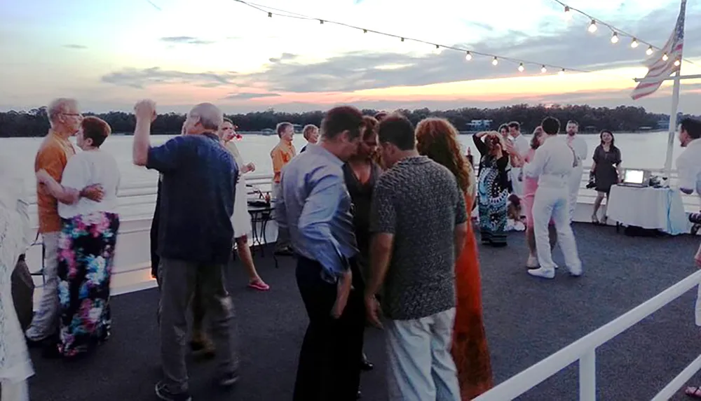 A group of people are enjoying a festive evening on a boat with a scenic sunset in the background