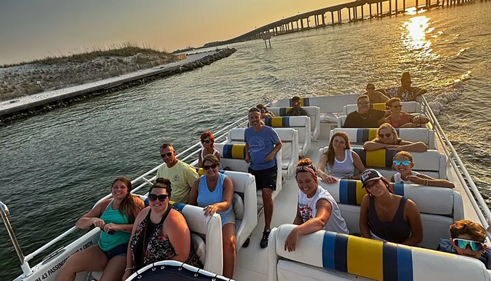 A group of people enjoy a boat tour as the sun sets creating a tranquil scene on the water with a bridge in the background