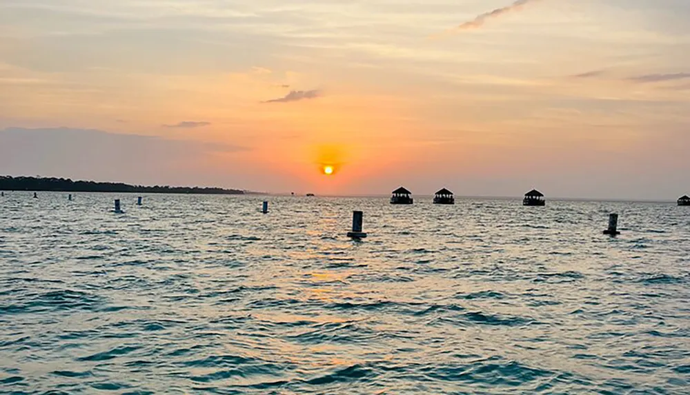 The image shows a tranquil ocean at sunset with remnants of old piers or docks dotting the horizon under a gradient sky