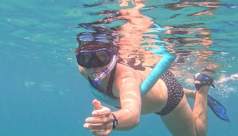 A person is snorkeling in clear blue water equipped with a snorkel mask and fins