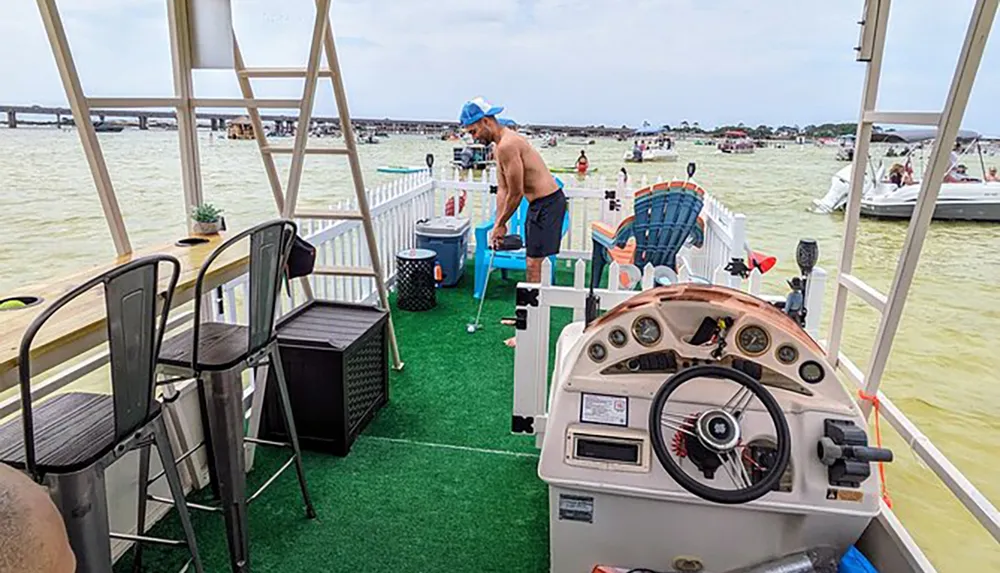 A person is practicing their golf swing on a grass-covered pontoon boat equipped with a patio set and lounge chairs surrounded by other watercraft on a busy waterway