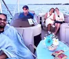 A group of people are enjoying a boat ride with a couple snuggled under a blanket in the foreground and two women sitting with snacks at a table while a man pilots the boat in the background