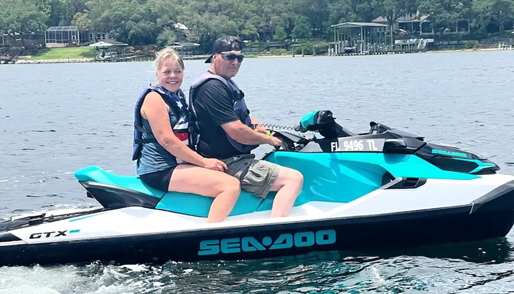 Two people are smiling and enjoying a ride on a Sea-Doo personal watercraft on a sunny day