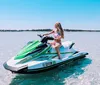 A person is energetically posing with a peace sign while seated on a green and white Yamaha WaveRunner on the water