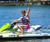 A person is energetically posing with a peace sign while seated on a green and white Yamaha WaveRunner on the water