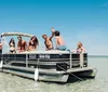 A group of friends is enjoying a sunny day on a pontoon boat waving and smiling with clear blue skies and water in the background